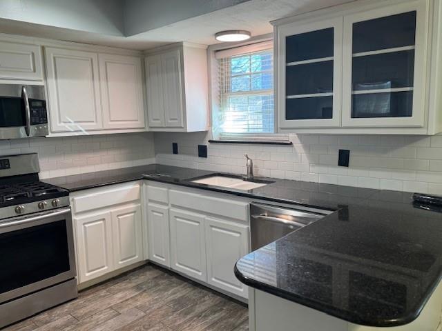 kitchen with dark wood-style floors, glass insert cabinets, appliances with stainless steel finishes, white cabinetry, and a sink