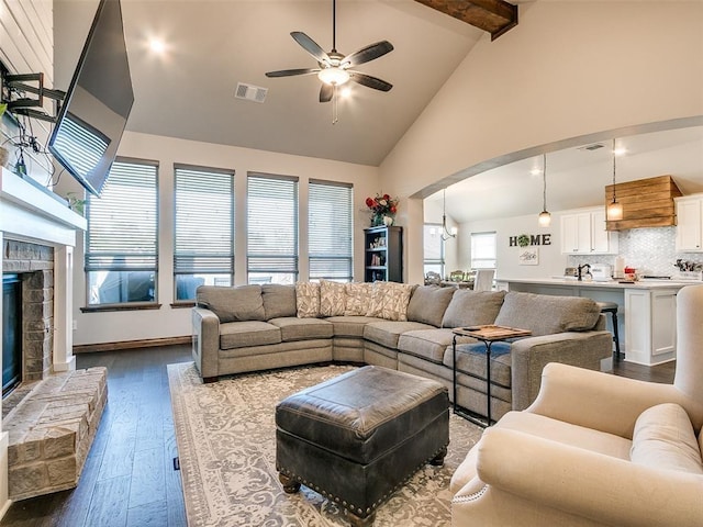 living room with ceiling fan, wood-type flooring, beam ceiling, high vaulted ceiling, and a fireplace