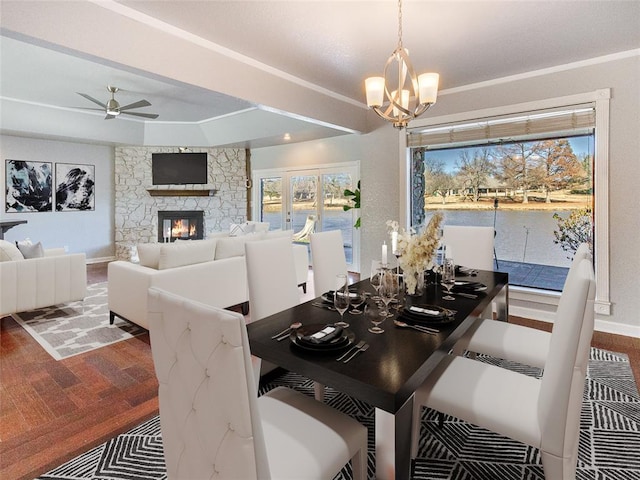 dining space with ceiling fan with notable chandelier, hardwood / wood-style flooring, and a stone fireplace