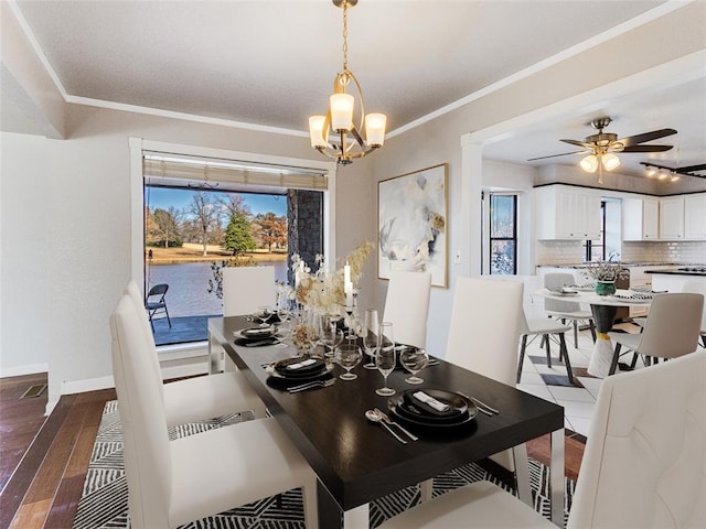 dining space featuring a water view, dark wood-type flooring, ornamental molding, and ceiling fan with notable chandelier