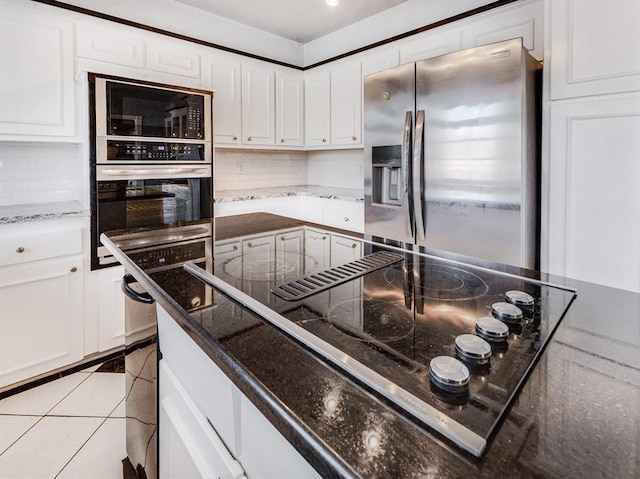 kitchen with black appliances, light tile patterned floors, dark stone counters, and white cabinetry