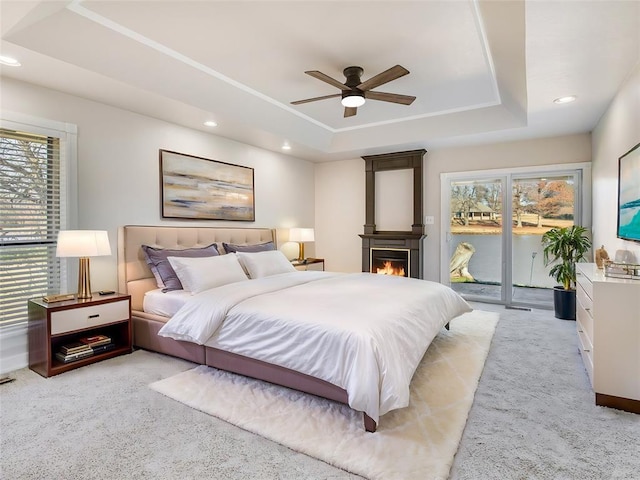 2207 Lake Front Cir, Norman, OK 73069 - bedroom featuring a tray ceiling, access to outside, light carpet, recessed lighting, and a lit fireplace