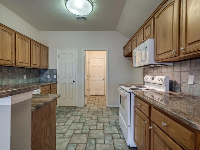 kitchen featuring tasteful backsplash, dark stone countertops, lofted ceiling, and white appliances