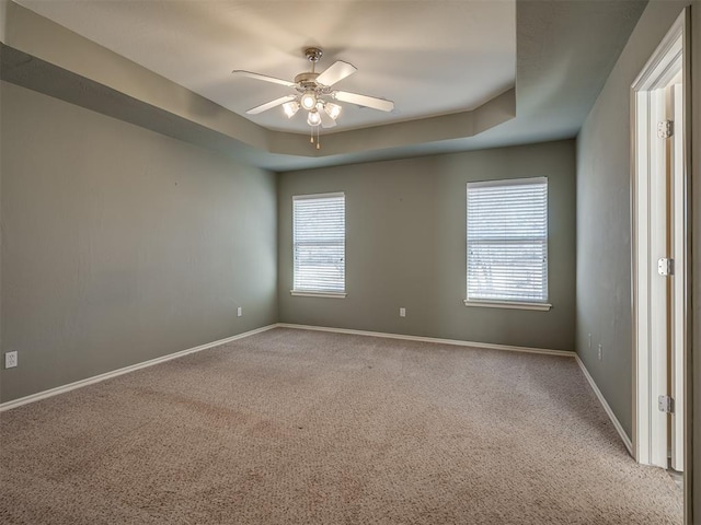 carpeted empty room featuring ceiling fan and a raised ceiling