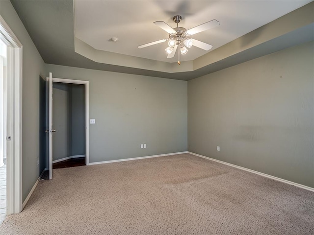 empty room featuring a tray ceiling, light carpet, and ceiling fan