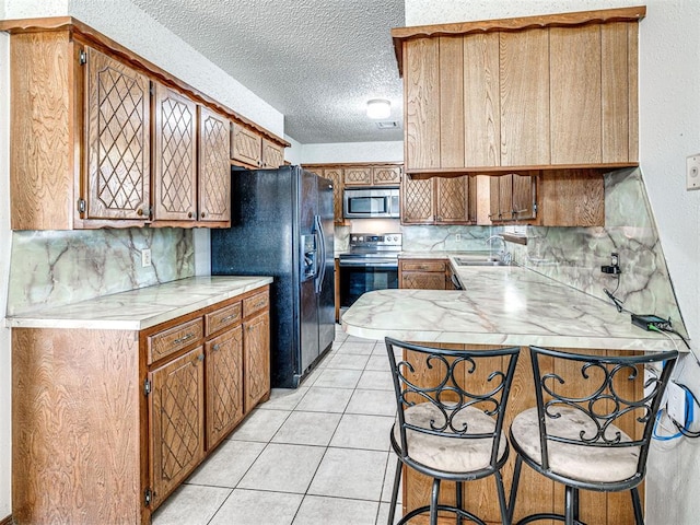 kitchen featuring kitchen peninsula, a kitchen breakfast bar, a textured ceiling, sink, and black appliances