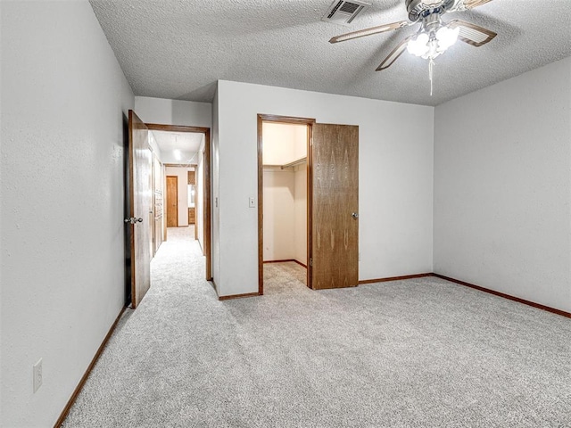 unfurnished bedroom with light carpet, a walk in closet, a textured ceiling, ceiling fan, and a closet