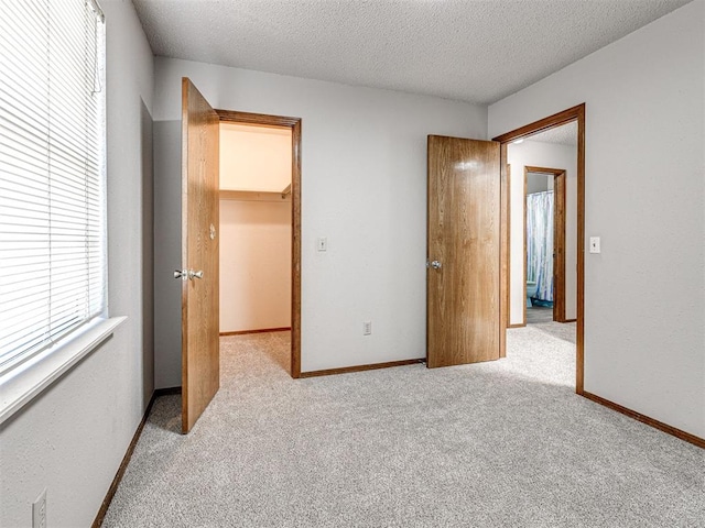 unfurnished bedroom featuring a walk in closet, light carpet, a closet, and a textured ceiling