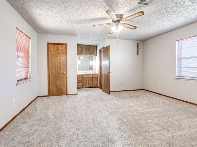 unfurnished bedroom featuring ensuite bath, ceiling fan, light colored carpet, and a textured ceiling