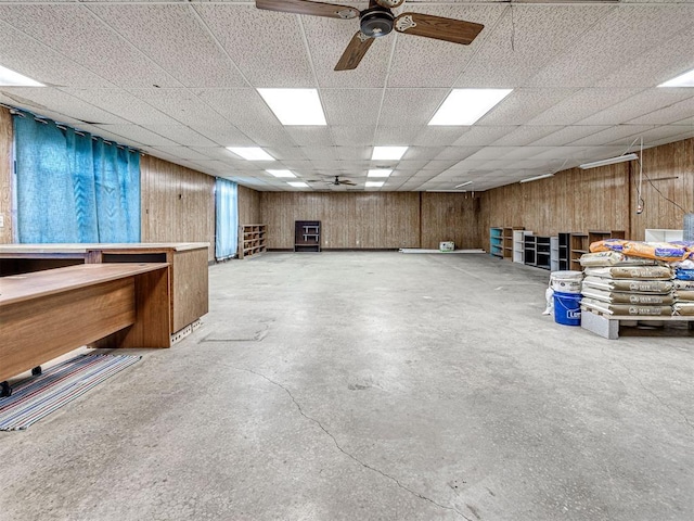 basement featuring ceiling fan, a drop ceiling, and wooden walls