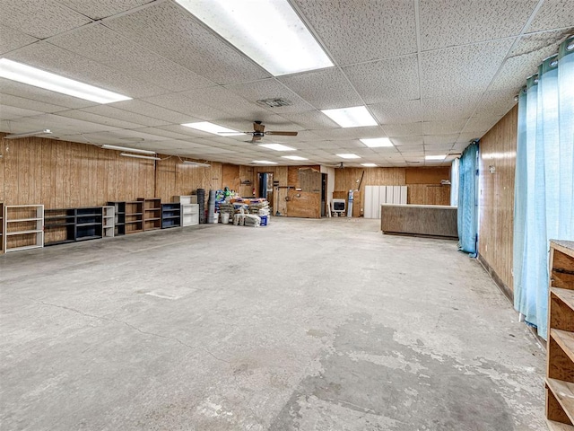 miscellaneous room featuring wood walls, a drop ceiling, ceiling fan, and concrete flooring