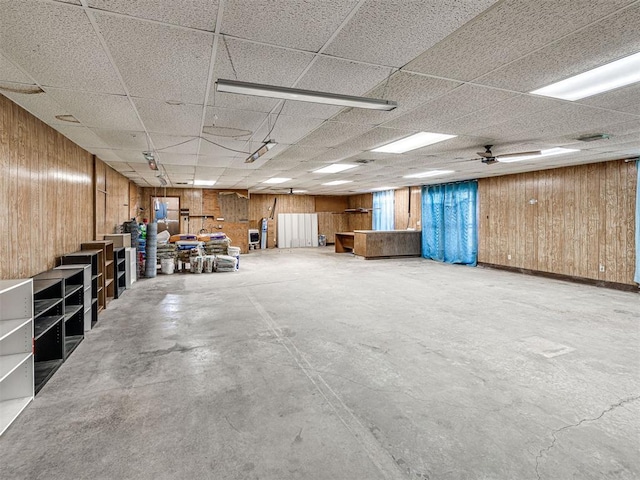 miscellaneous room with a paneled ceiling, wooden walls, ceiling fan, and concrete floors