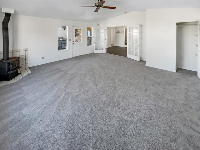 unfurnished living room featuring a wood stove, ceiling fan, dark carpet, and lofted ceiling