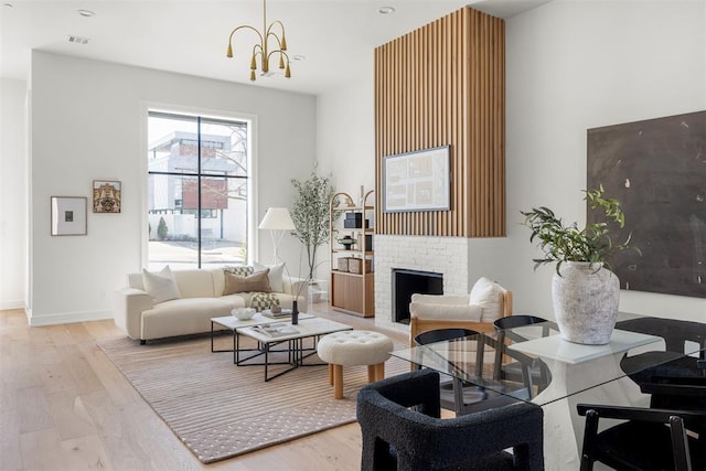 living room featuring light wood-type flooring, a brick fireplace, and a notable chandelier