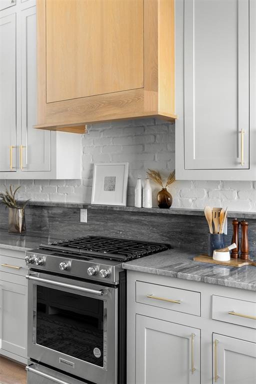 kitchen featuring decorative backsplash, stainless steel stove, light stone counters, and white cabinets