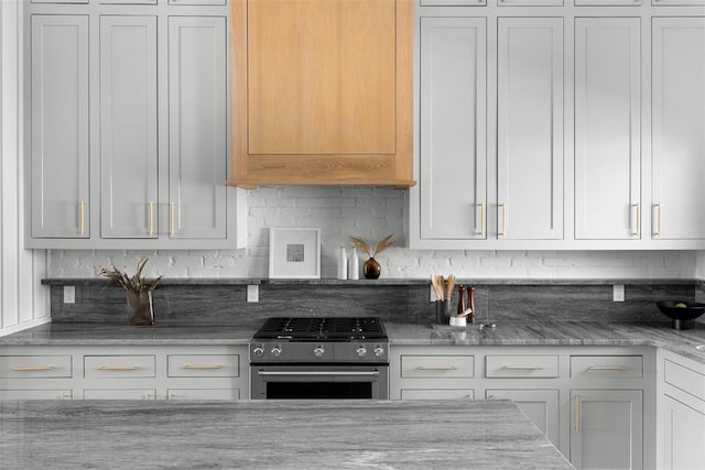 kitchen with white cabinets, decorative backsplash, stainless steel gas range oven, and light stone counters