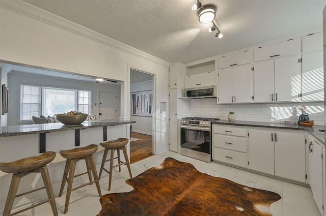 kitchen with white cabinetry, stainless steel appliances, kitchen peninsula, a kitchen bar, and decorative backsplash