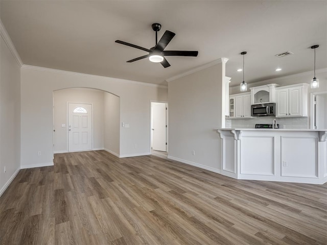 unfurnished living room featuring light hardwood / wood-style floors, ceiling fan, and ornamental molding