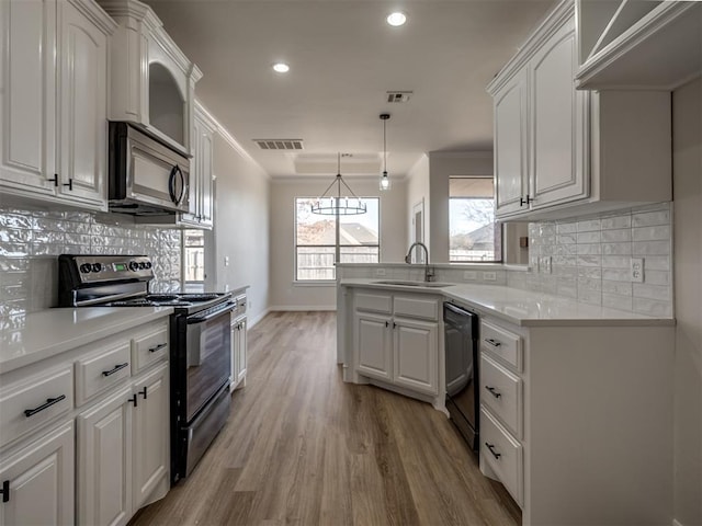 kitchen featuring light wood-type flooring, sink, black appliances, decorative light fixtures, and white cabinetry