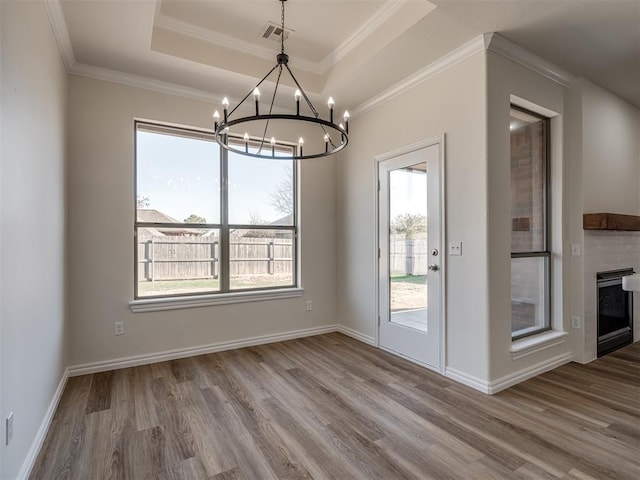 unfurnished dining area with a tray ceiling, ornamental molding, a chandelier, and light wood-type flooring
