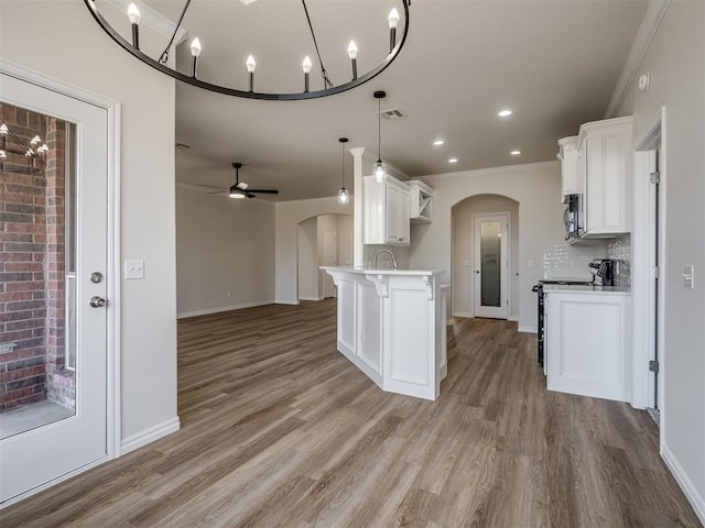 kitchen featuring decorative backsplash, light wood-type flooring, ceiling fan with notable chandelier, decorative light fixtures, and white cabinetry