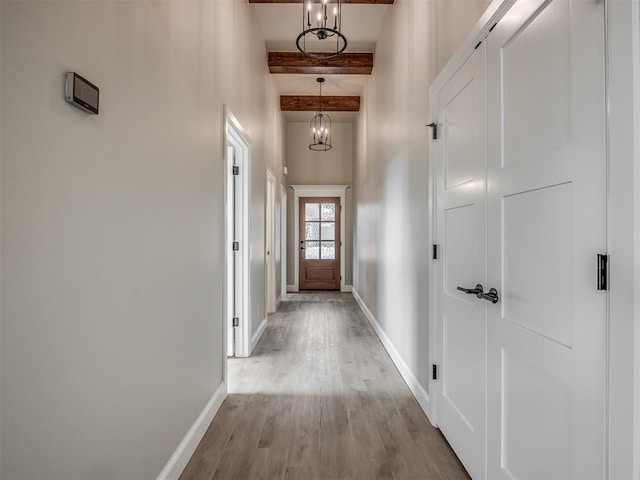 hall featuring a towering ceiling, beamed ceiling, a chandelier, and light hardwood / wood-style floors