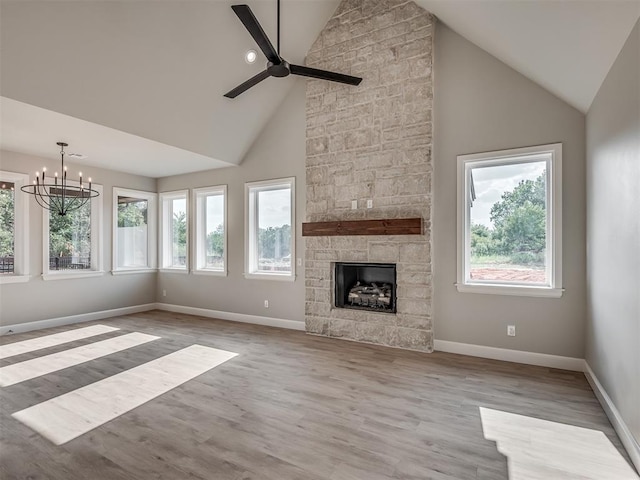 unfurnished living room featuring ceiling fan with notable chandelier, a stone fireplace, light wood-type flooring, and high vaulted ceiling