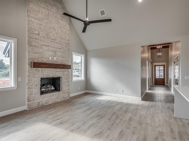 unfurnished living room with a fireplace, ceiling fan with notable chandelier, light hardwood / wood-style flooring, and high vaulted ceiling