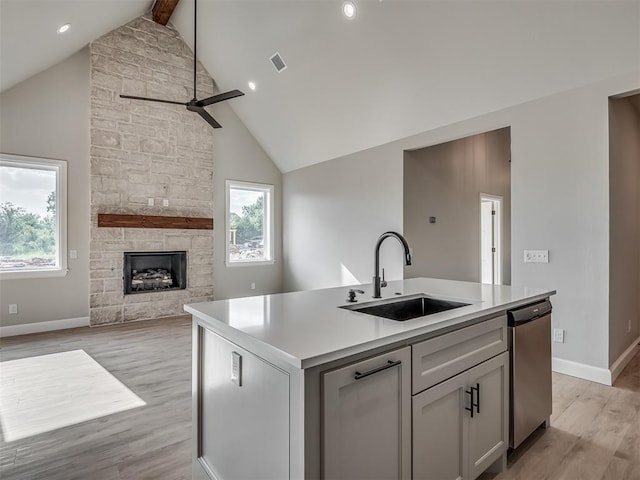 kitchen featuring sink, light hardwood / wood-style flooring, stainless steel dishwasher, an island with sink, and a fireplace