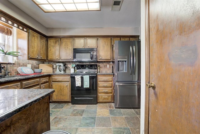 kitchen featuring sink, dark stone counters, black appliances, and decorative backsplash