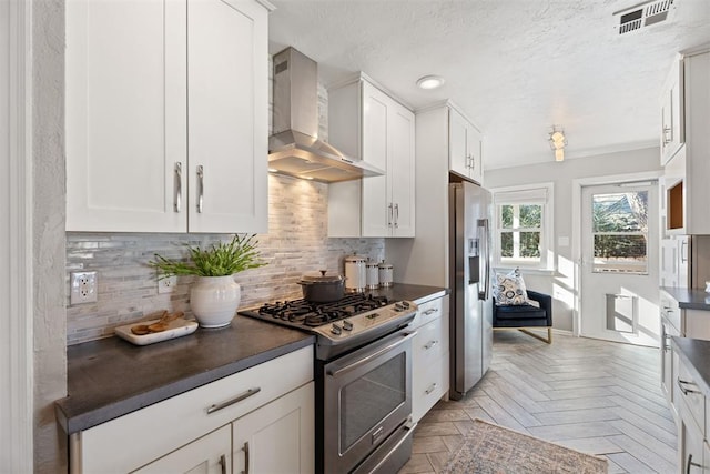 kitchen featuring white cabinets, wall chimney exhaust hood, appliances with stainless steel finishes, and light parquet floors