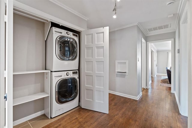 clothes washing area featuring crown molding, track lighting, stacked washer / drying machine, and hardwood / wood-style flooring