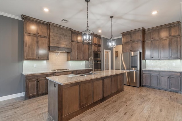 kitchen with appliances with stainless steel finishes, sink, pendant lighting, a center island with sink, and light hardwood / wood-style flooring