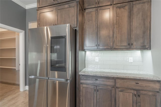 kitchen featuring stainless steel fridge, decorative backsplash, ornamental molding, light hardwood / wood-style floors, and light stone countertops