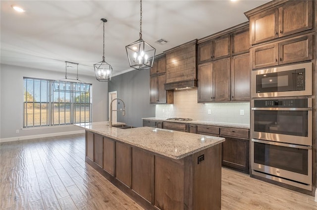 kitchen with sink, decorative light fixtures, stainless steel appliances, light stone countertops, and a kitchen island with sink