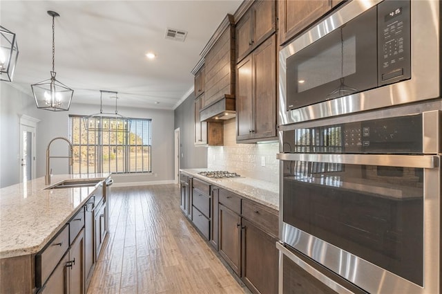 kitchen featuring decorative light fixtures, built in microwave, tasteful backsplash, sink, and a center island with sink