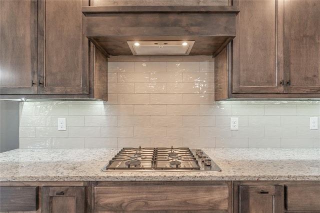 kitchen featuring light stone counters, tasteful backsplash, stainless steel gas cooktop, and custom range hood