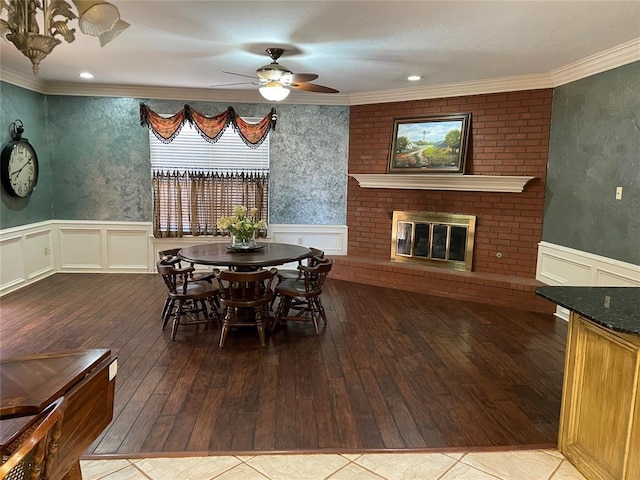 dining space featuring hardwood / wood-style floors, a brick fireplace, ornamental molding, and ceiling fan