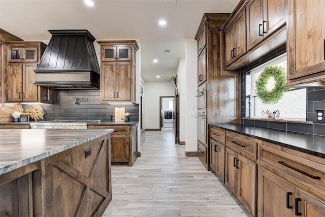 kitchen with light hardwood / wood-style flooring, double oven, stove, decorative backsplash, and custom exhaust hood