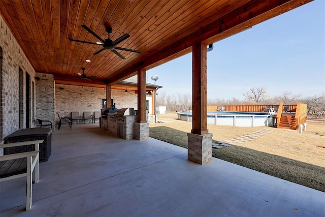 view of patio featuring a grill, ceiling fan, an outdoor kitchen, and an empty pool