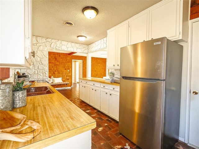 kitchen with white cabinetry, stainless steel refrigerator, a textured ceiling, and kitchen peninsula