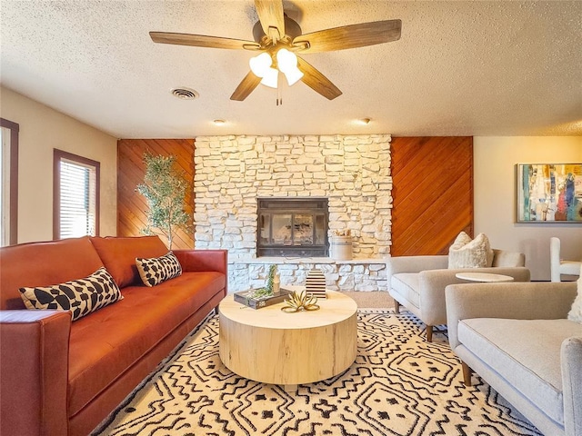 living room with wood walls, ceiling fan, a textured ceiling, and a stone fireplace