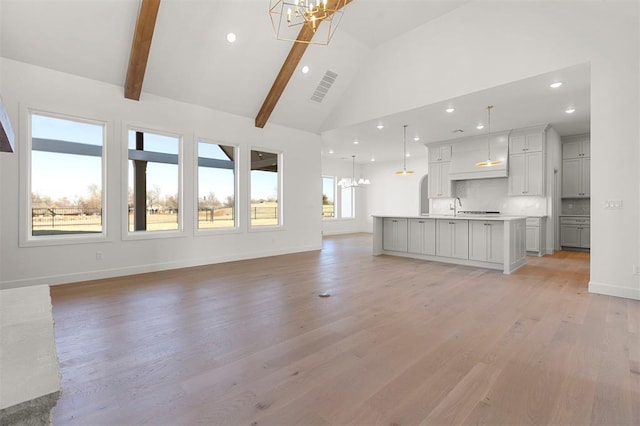 unfurnished living room featuring beamed ceiling, light wood-type flooring, an inviting chandelier, and high vaulted ceiling