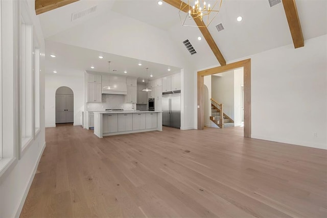 unfurnished living room featuring a chandelier, beamed ceiling, light wood-type flooring, and high vaulted ceiling