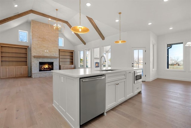 kitchen featuring a kitchen island with sink, white cabinets, sink, stainless steel dishwasher, and decorative light fixtures