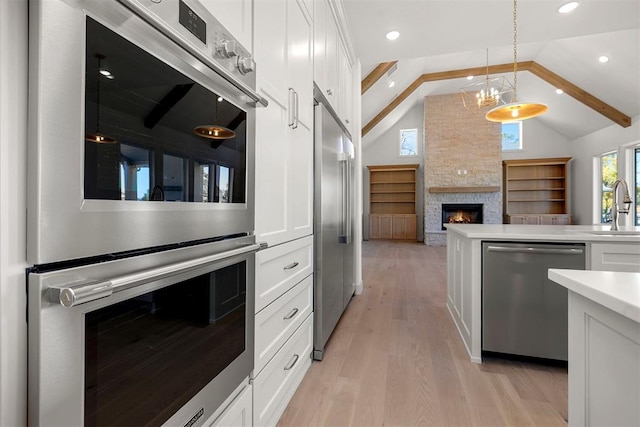 kitchen with appliances with stainless steel finishes, vaulted ceiling with beams, white cabinetry, and pendant lighting