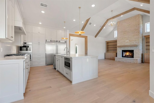 kitchen with pendant lighting, a stone fireplace, white cabinetry, and a kitchen island with sink