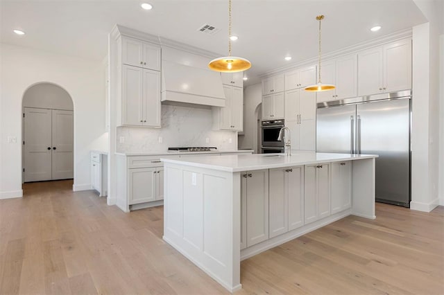 kitchen featuring appliances with stainless steel finishes, white cabinetry, pendant lighting, and an island with sink