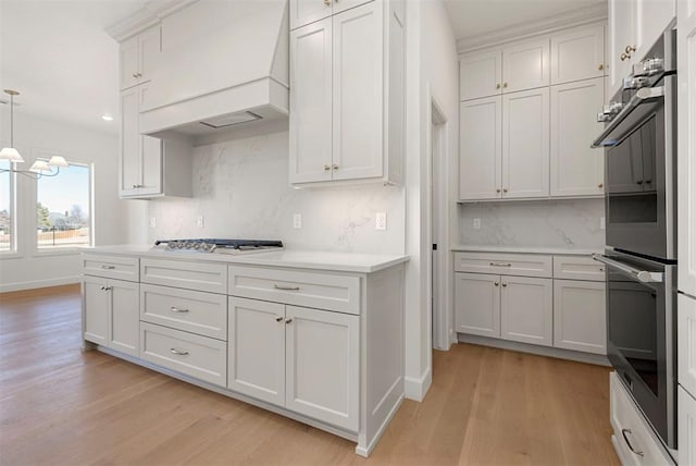 kitchen featuring backsplash, white cabinets, light wood-type flooring, decorative light fixtures, and custom range hood