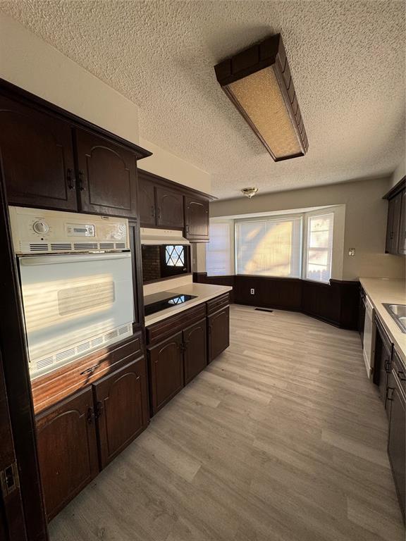 kitchen with oven, dark brown cabinets, a textured ceiling, and light hardwood / wood-style flooring